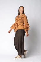 Woman wearing a brown ruffled blouse and dark pants on a white background