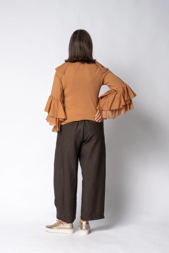 Person wearing a brown ruffled blouse and dark pants on a white background back angle