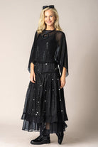 Woman wearing a black outfit with sheer sleeves and a long skirt against a beige background