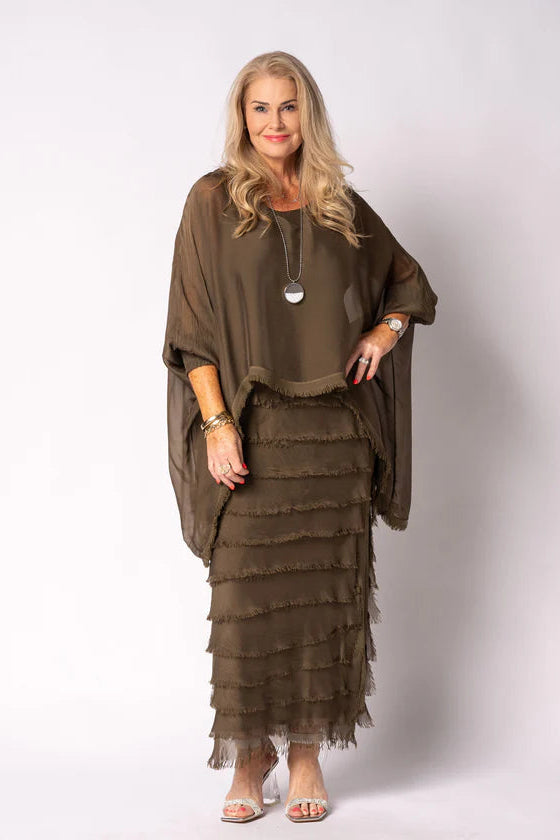 Woman wearing a moss green layered dress and poncho against a white background