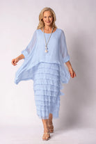 A woman modeling a light blue tiered maxi dress with a matching sheer long-sleeve top, standing against a light gray studio background.