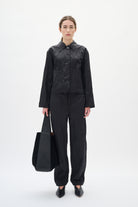 Person wearing a black outfit holding a black bag on a white background