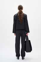 Person wearing a black suit holding a black bag on a white background back angle