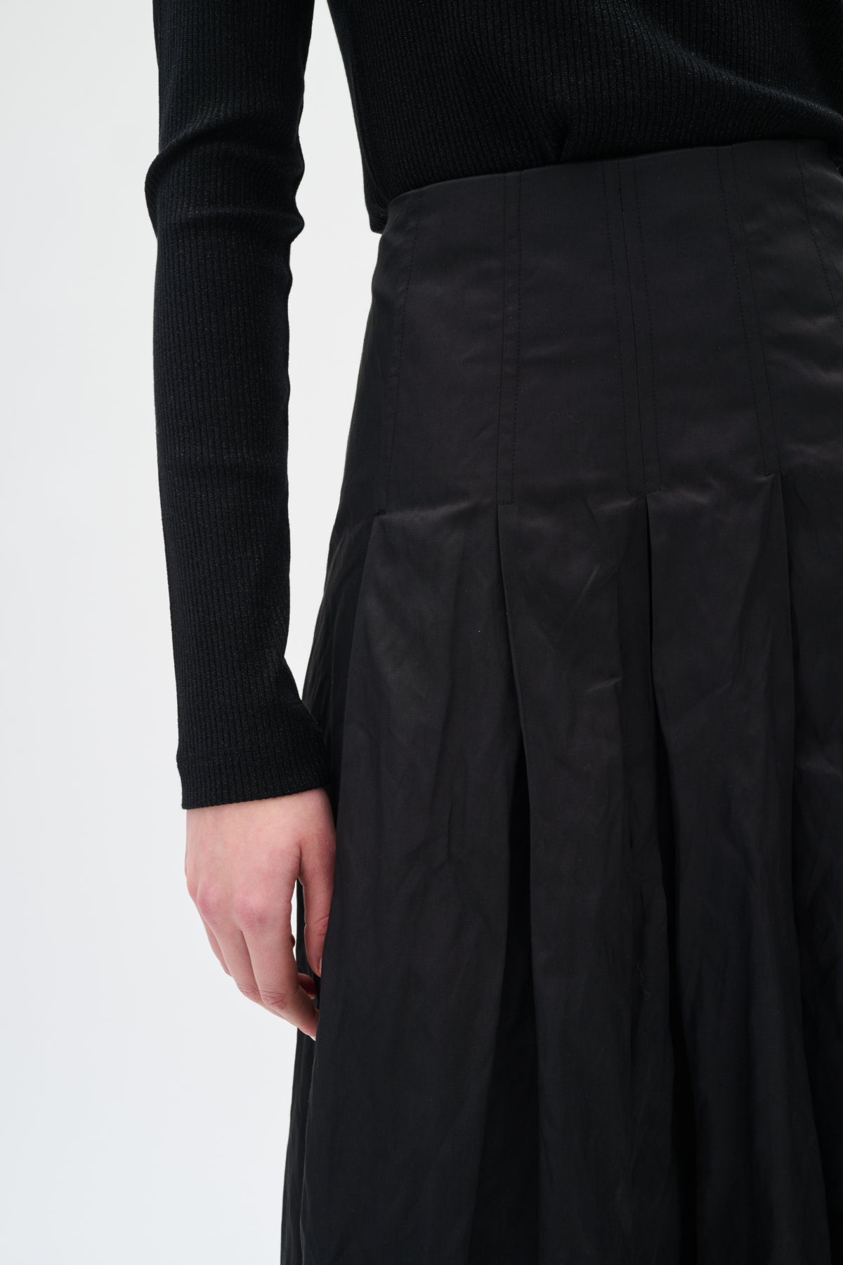 Person wearing a black pleated skirt and black long-sleeve top on a white background