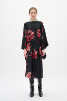 Woman wearing a black dress with red floral patterns on a white background
