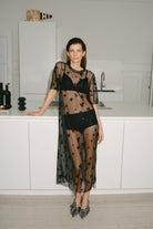 Woman wearing a sheer black dress with embellishments in a kitchen.