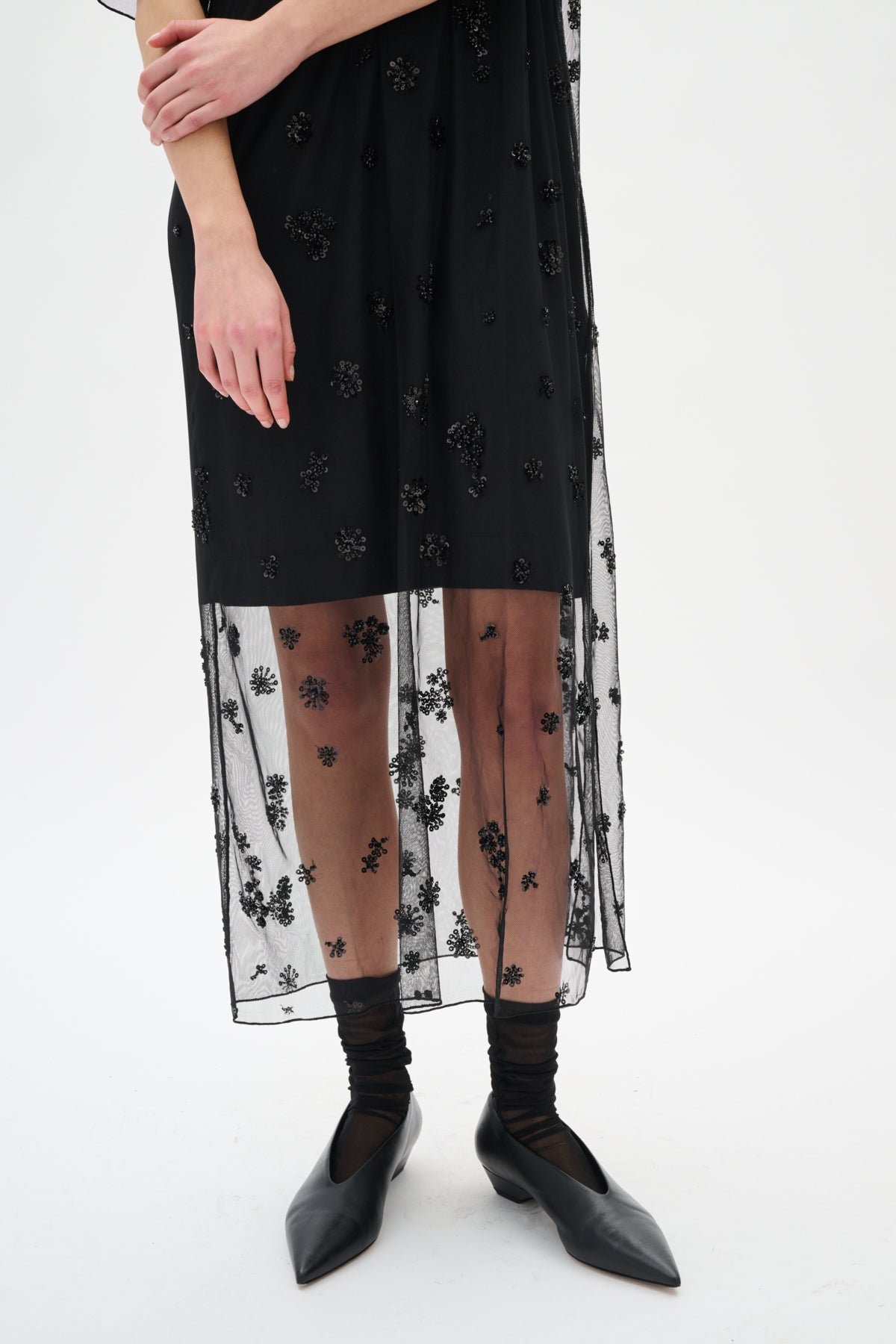 Black dress with floral embroidery, sheer overlay, black tights, and black shoes on a white background