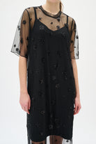Black dress with sheer sleeves and floral embellishments on a white background