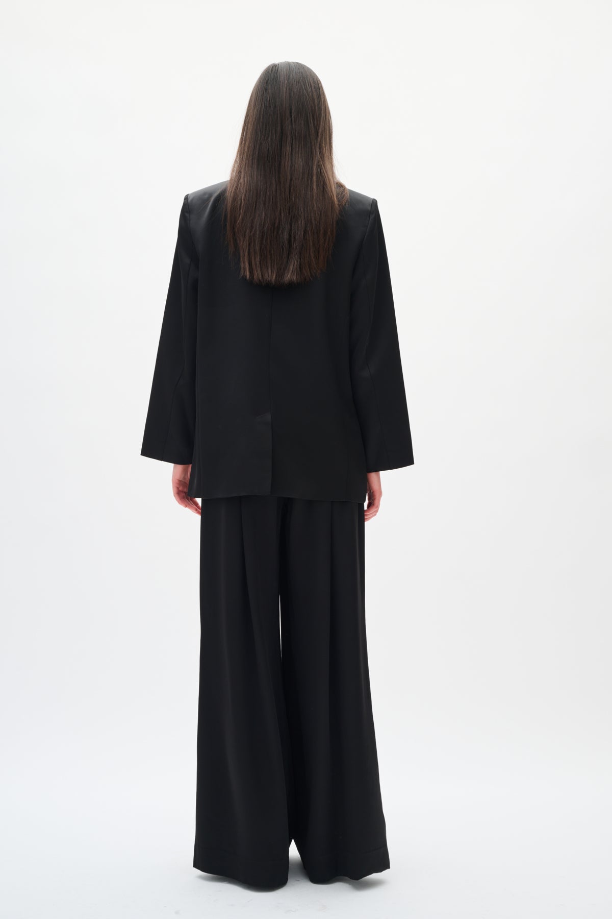 Person wearing a black suit standing against a white background back angle