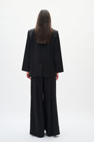 Person wearing a black suit standing against a white background back angle