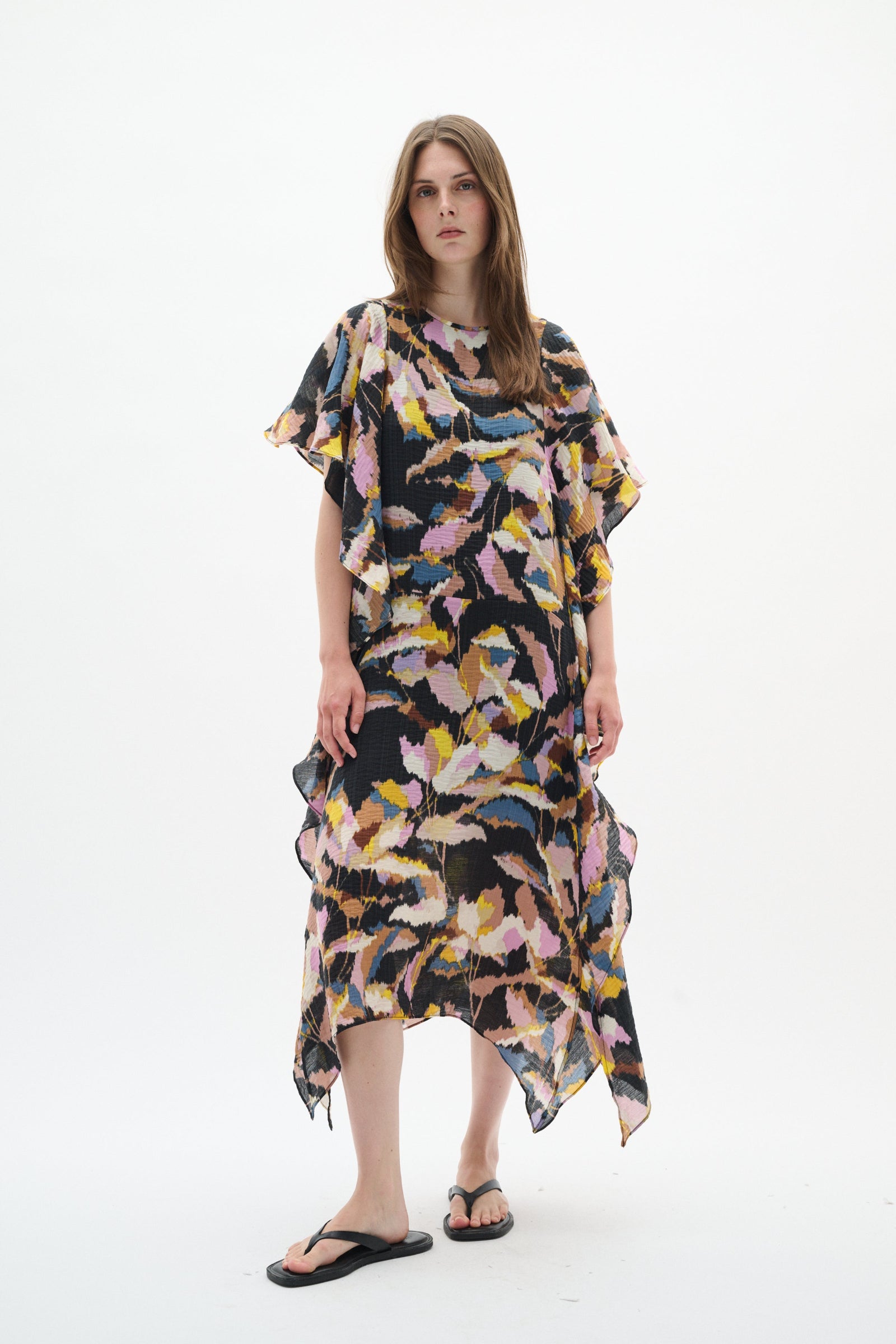 A woman modeling a loose, high-low ruffled dress with a multicolor abstract print on a solid white background.