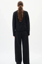 Woman wearing a black textured sweater and diamante black jeans on a white background back angle