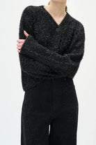 Woman wearing a black textured sweater and diamante black jeans on a white background
