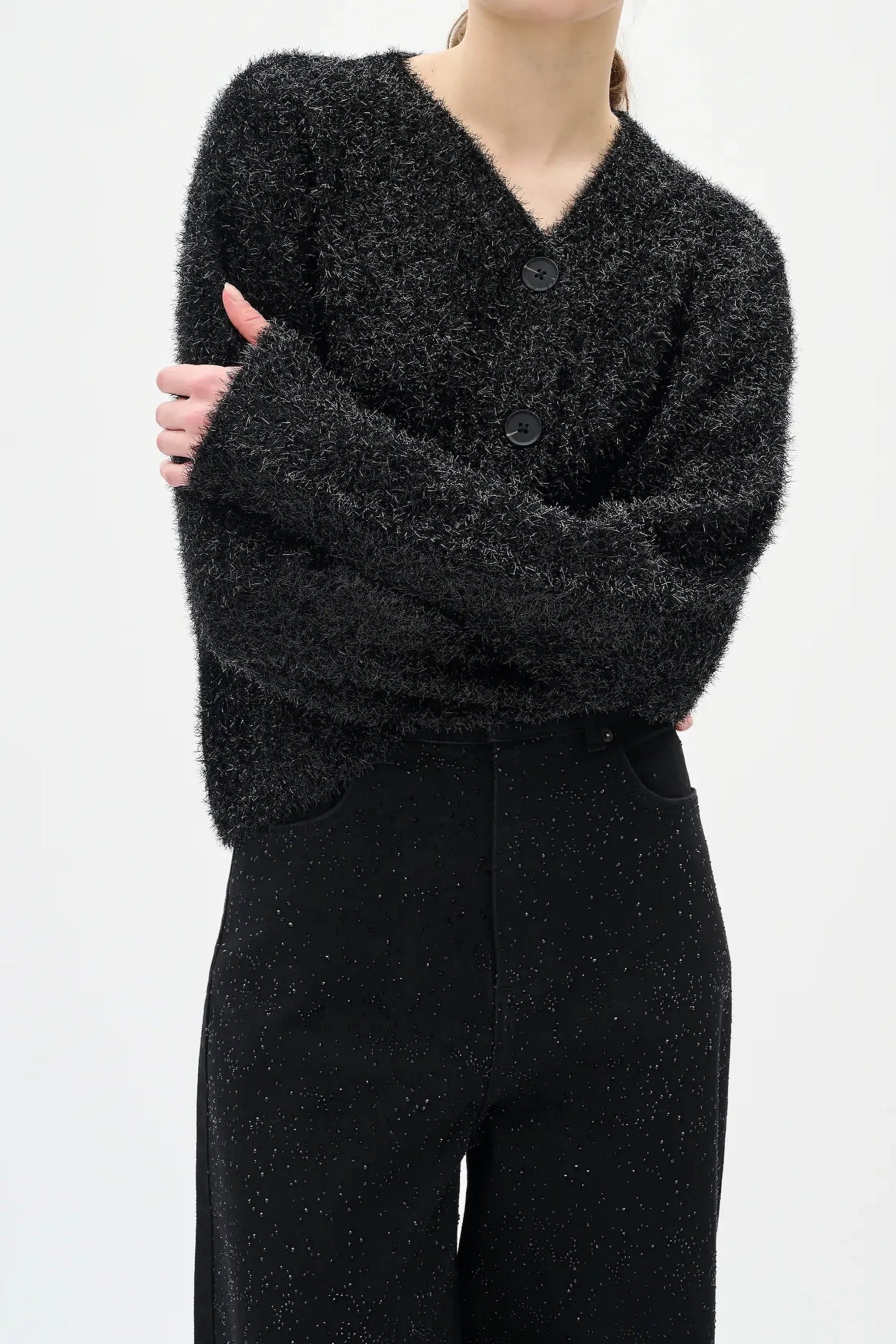 Woman wearing a black textured sweater and diamante black jeans on a white background