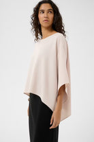 Woman wearing a beige poncho over a black outfit on a white background
