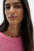 Close-up portrait of a woman wearing a pink knit crewneck sweater against a plain light background.