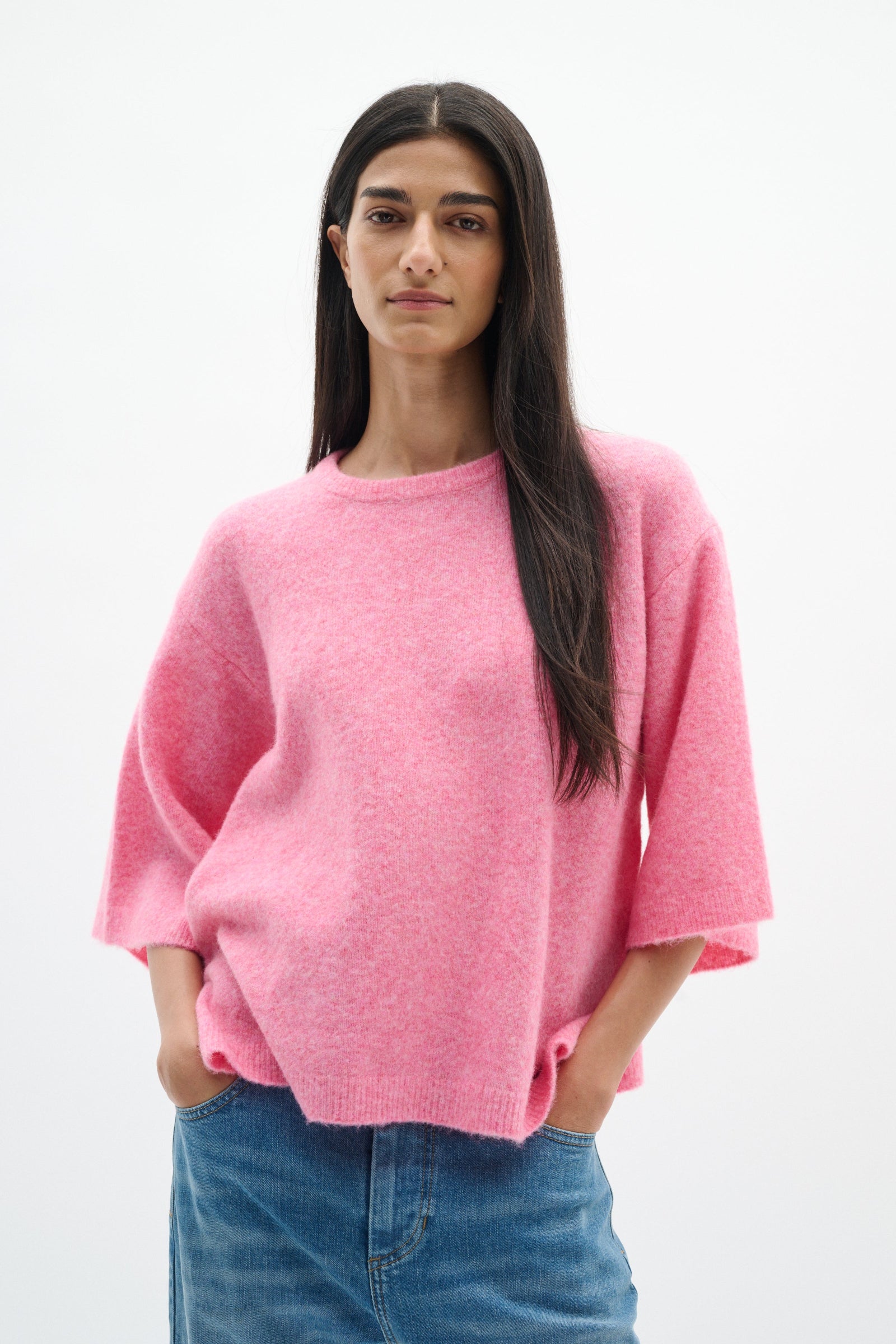 Woman wearing a pink sweater and blue jeans on a white background