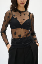 Black sheer top with floral embellishments worn by a model on a white background