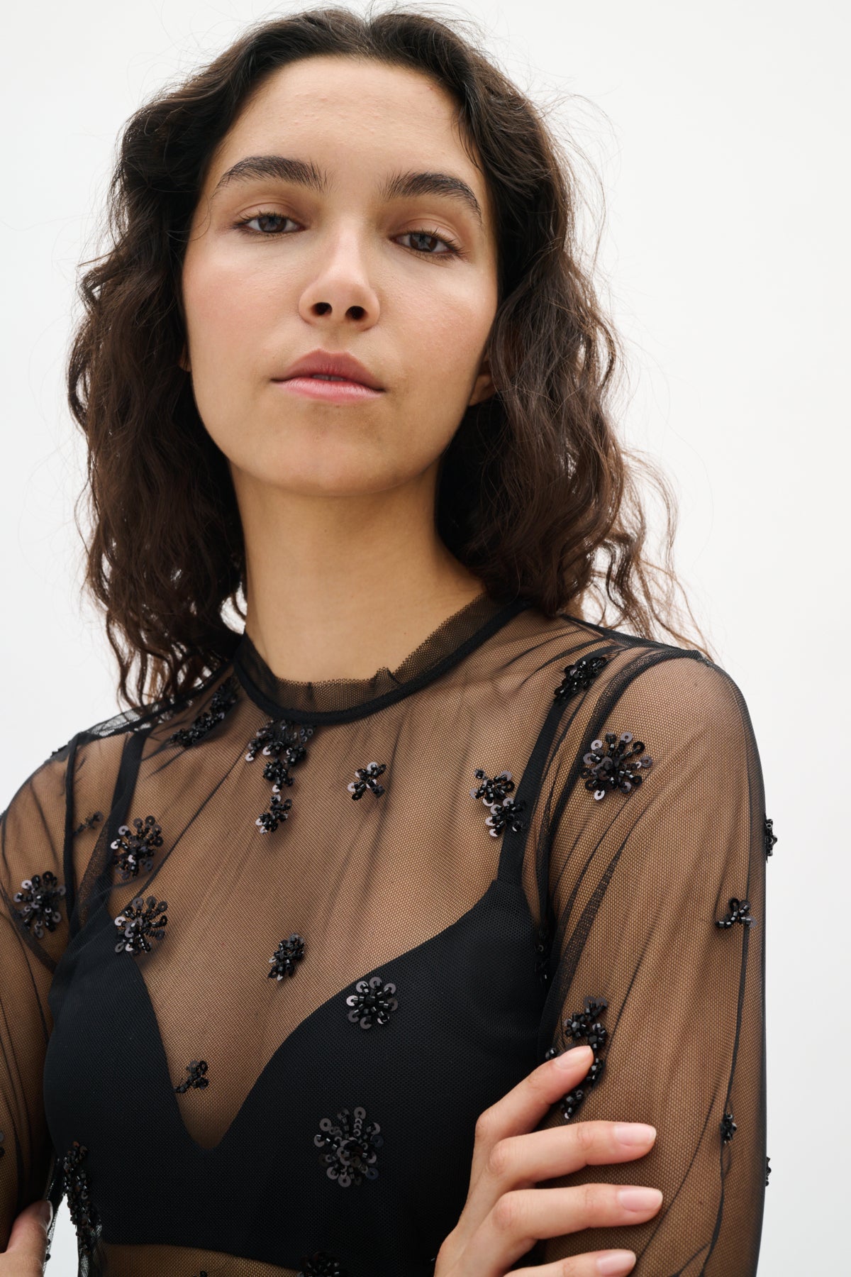 Woman wearing a black sheer top with floral embellishments on a white background
