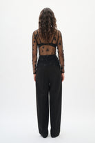 Person wearing a sheer top with black polka dots and high-waisted black pants on a white background back angle