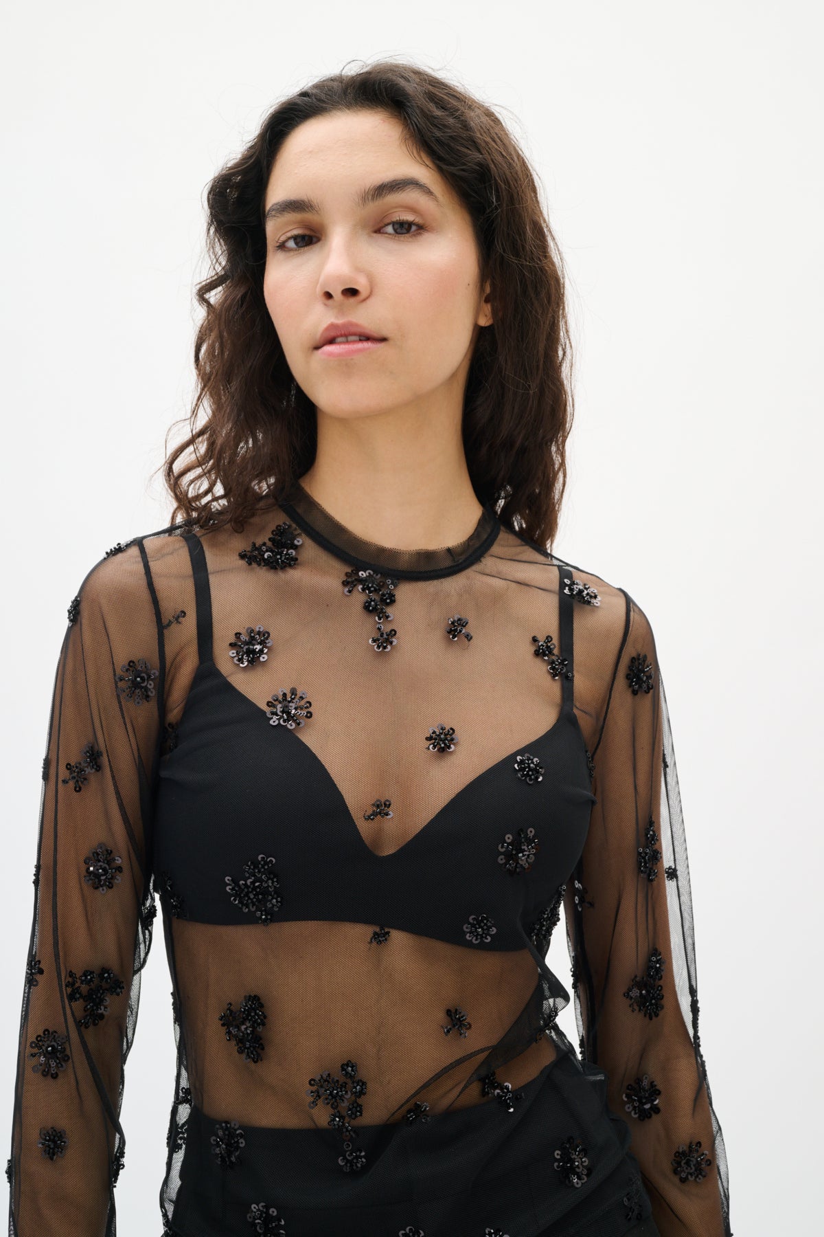 Woman wearing a black embroidered top with sheer sleeves on a white background