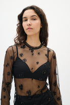 Woman wearing a black embroidered top with sheer sleeves on a white background