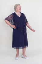 Person wearing a navy blue beaded dress with sheer sleeves on a white background