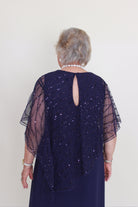 Person wearing a dark blue dress with sheer sleeves on a white background