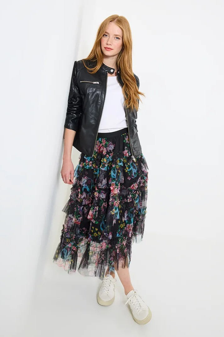 Woman wearing a black leather jacket, white top, and floral skirt on a white background