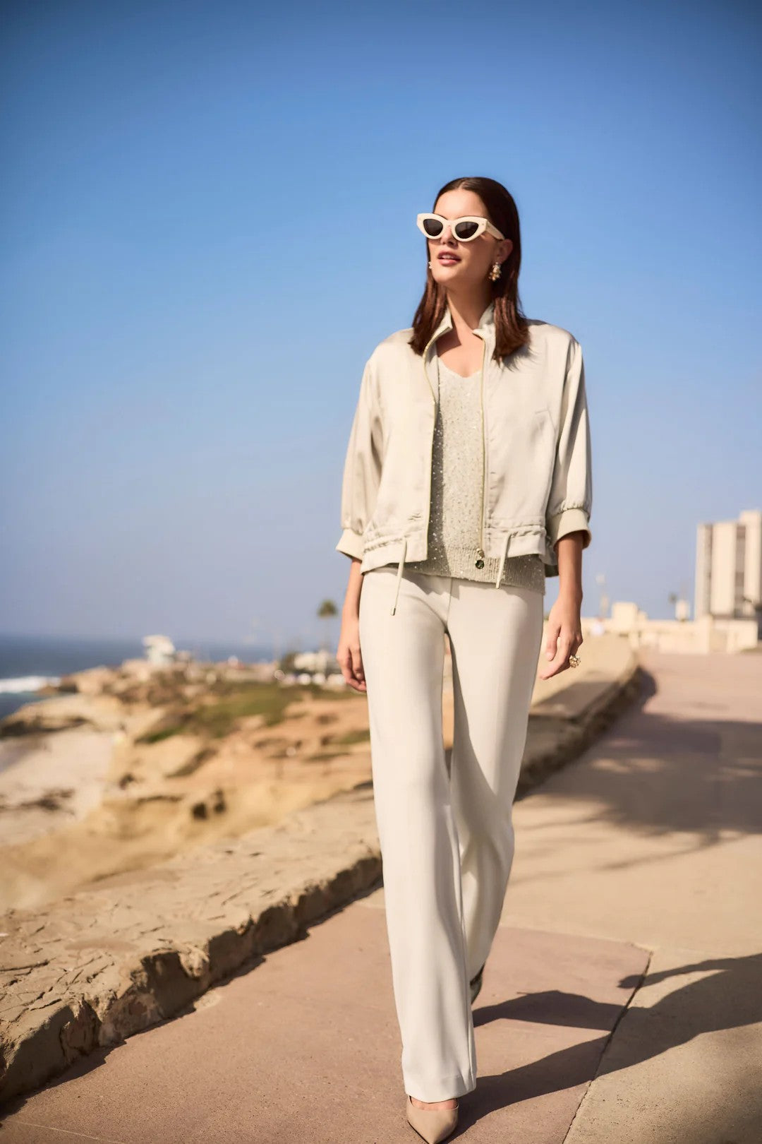Woman in light-colored outfit walking along a coastal path with clear blue sky.
