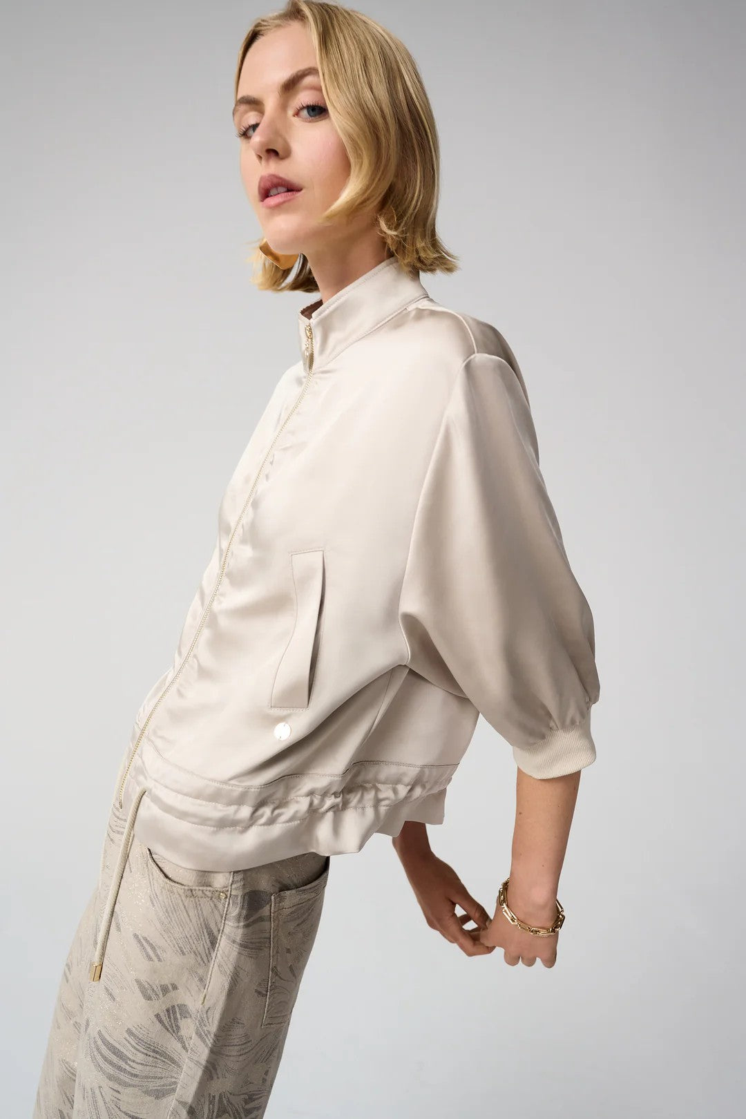 Woman wearing a beige satin jacket and pants on a white background side angle