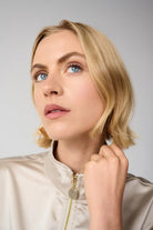 close up of a woman wearing a beige jacket against a gray background