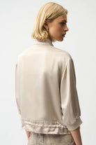 Woman wearing a beige satin jacket and pants on a white background back angle