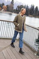 Person wearing olive jacket on a wooden deck by a lake with mountains in the background