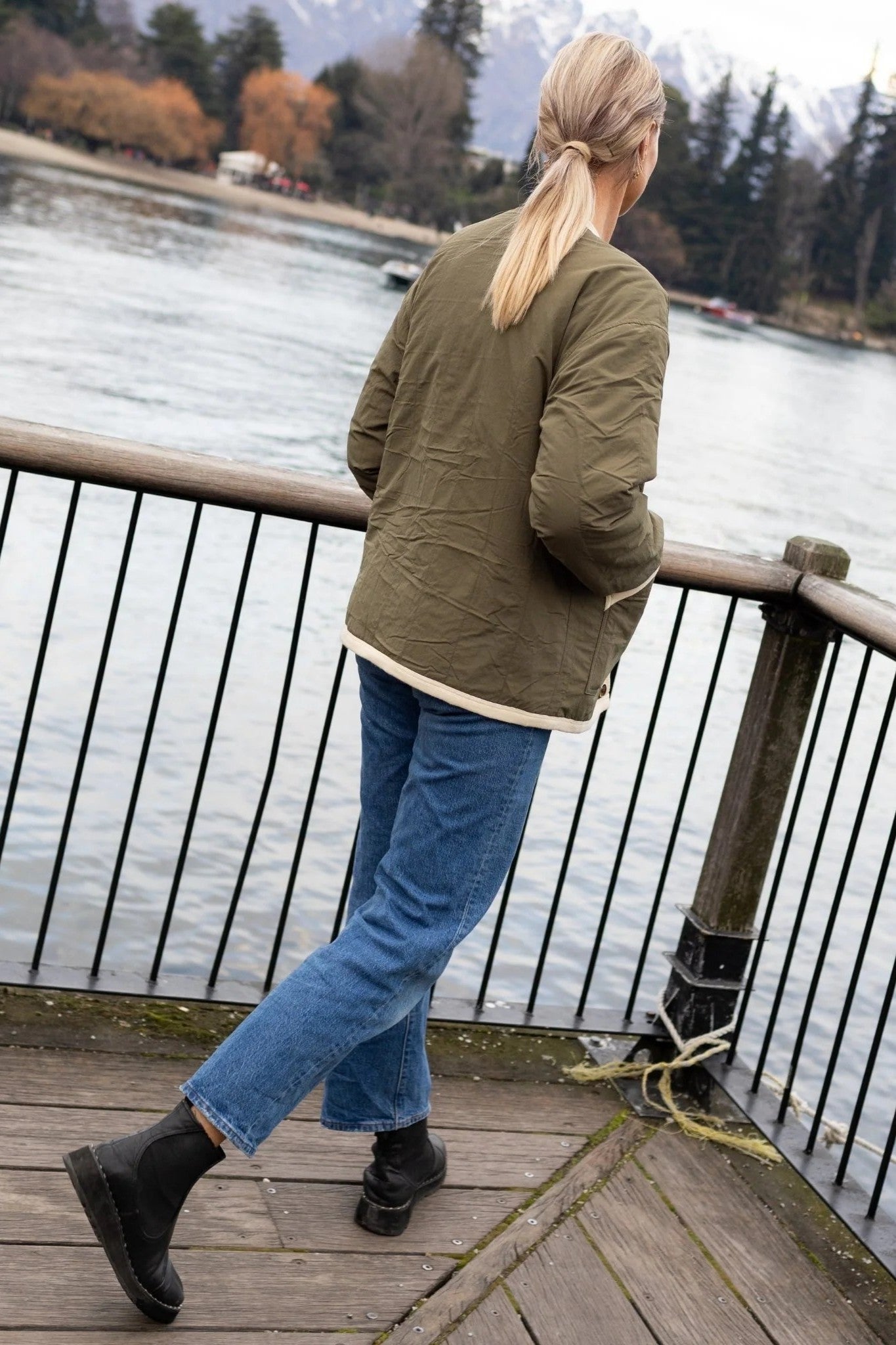 woman standing outdoors wearing olive green jacket and jeans back angle 