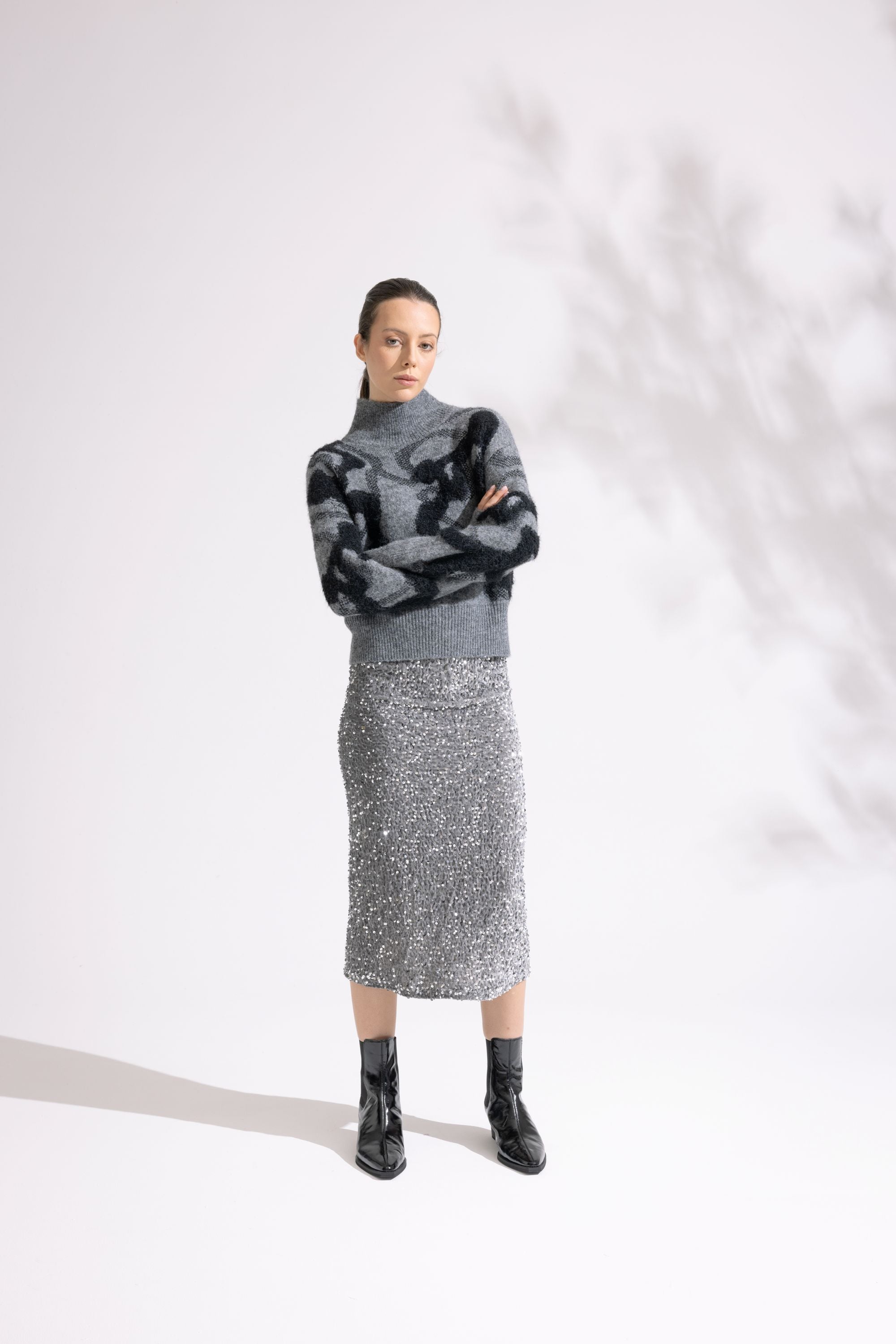 Person wearing a patterned sweater, gray turtleneck, sequin skirt, and black boots on a white background