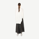 Woman wearing a white top with branch print and a long black skirt on a white background back angle