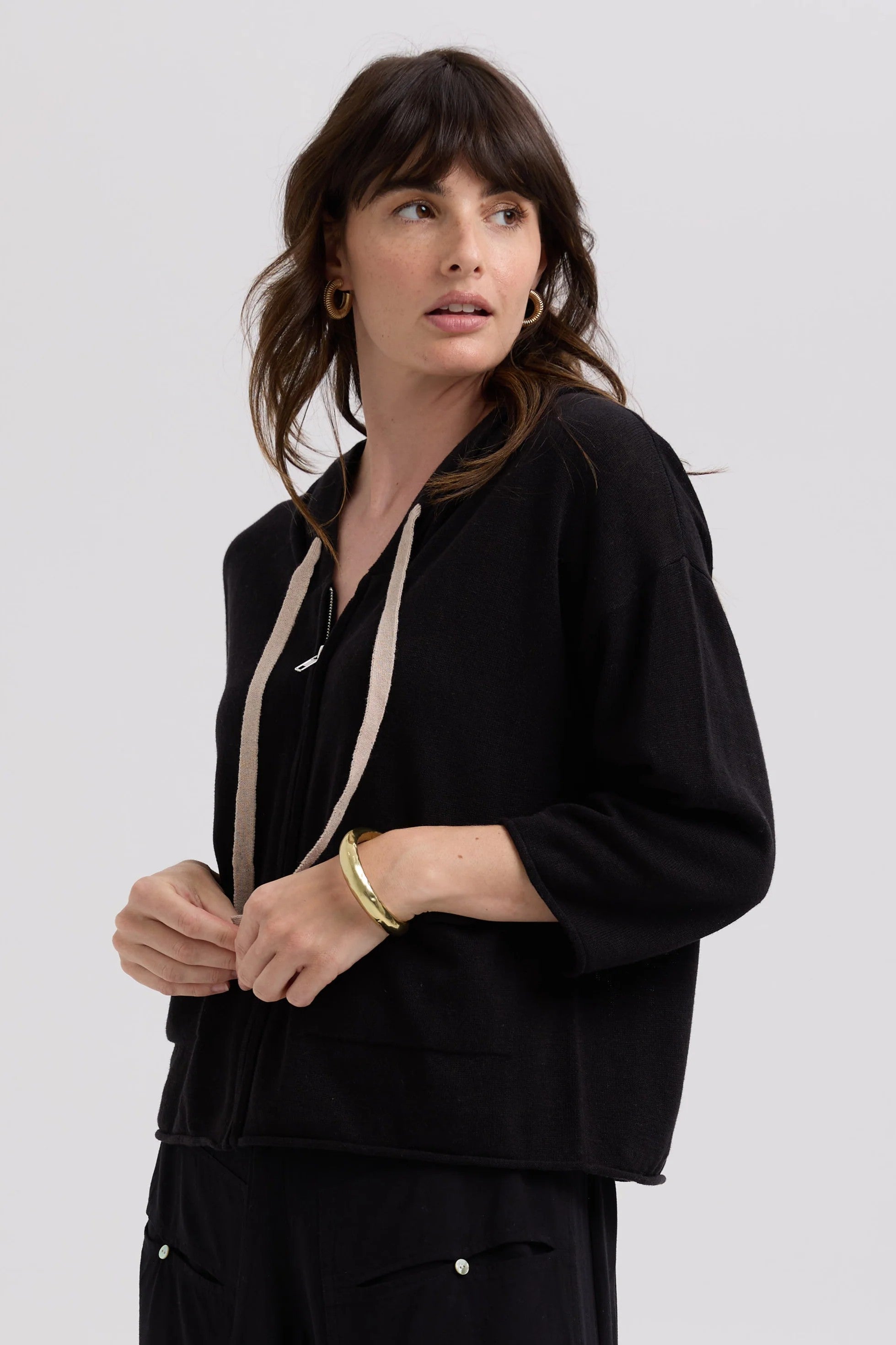 Woman wearing a black outfit with a beige strap against a white background