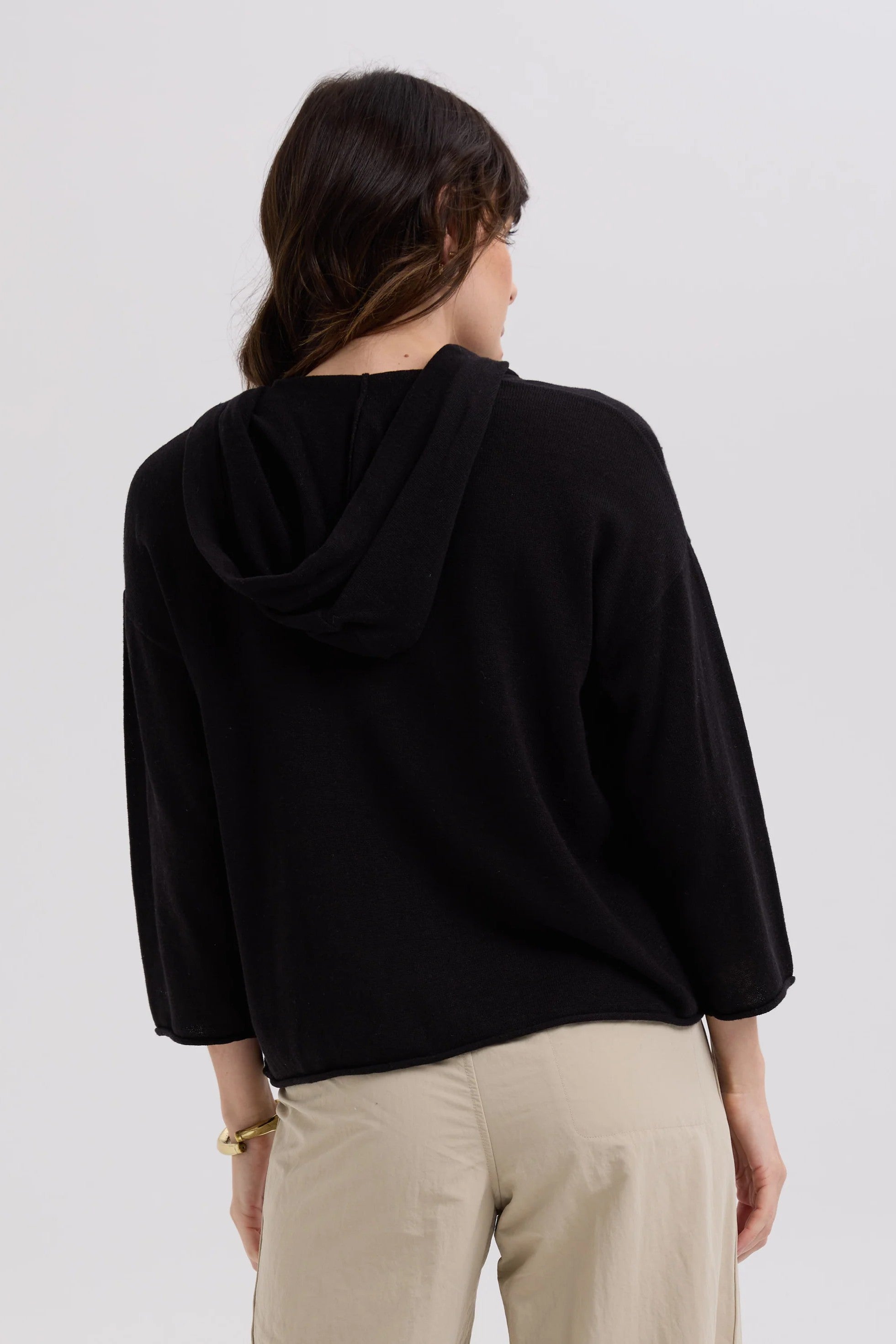 Person wearing a black hoodie and beige pants on a white background