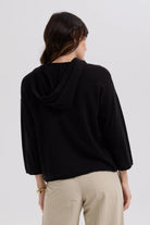 Person wearing a black hoodie and beige pants on a white background