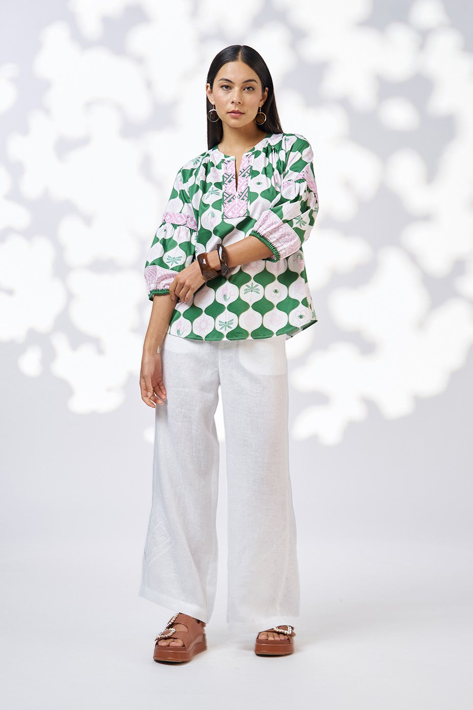 model wearing green white and pink patterned blouse and white pant
