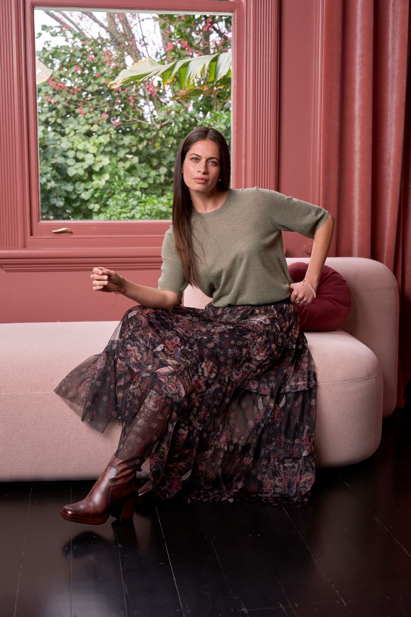 Woman sitting on a pink couch in a room with pink walls and a window.