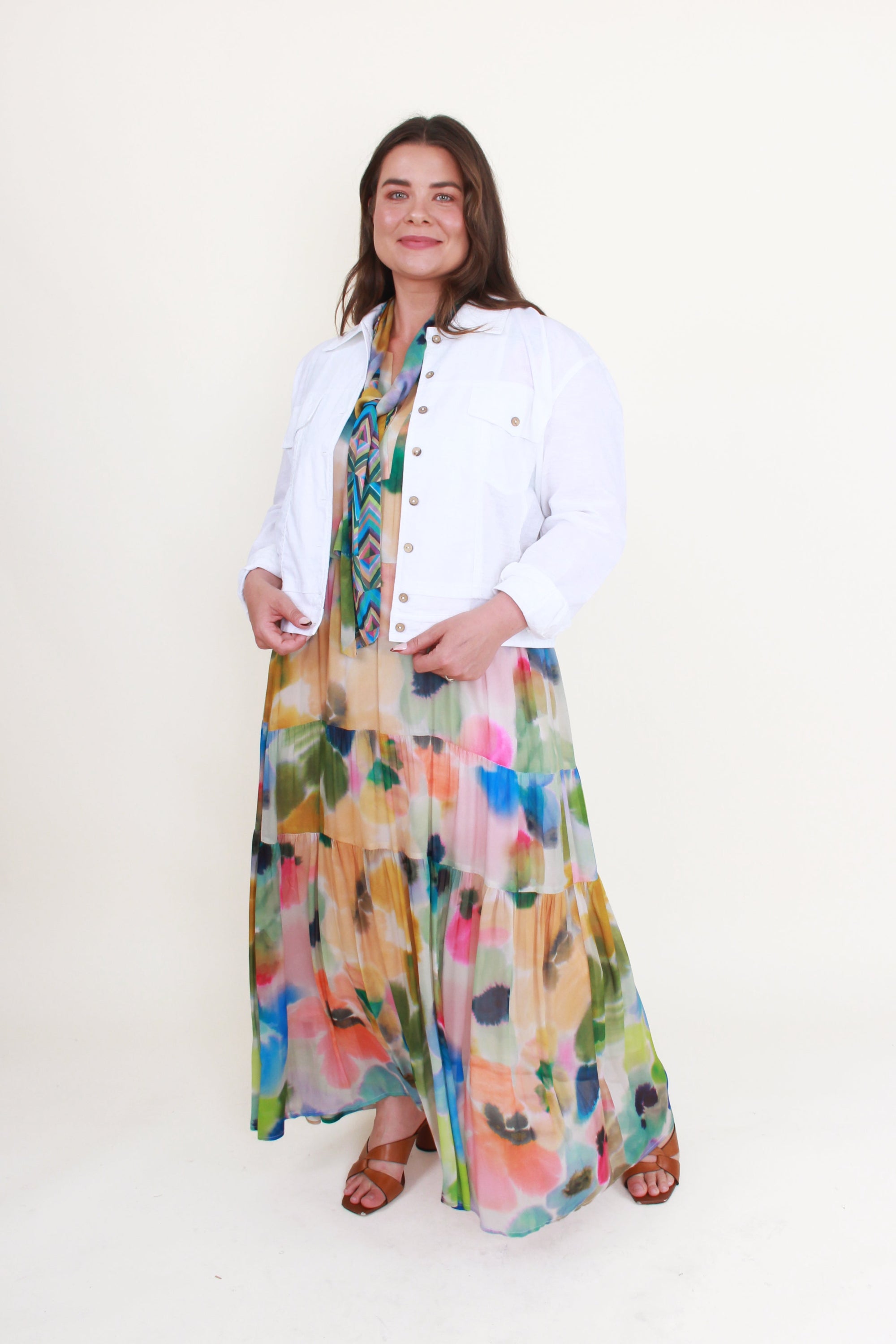 Woman wearing a white jacket and colorful floral dress on a white background