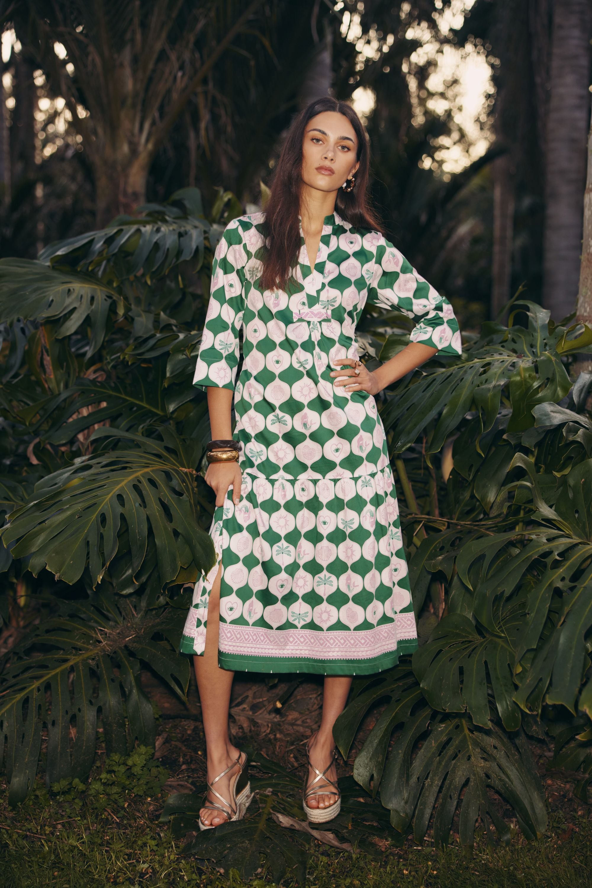 model wearing green and white midi dress standing among tropical plants