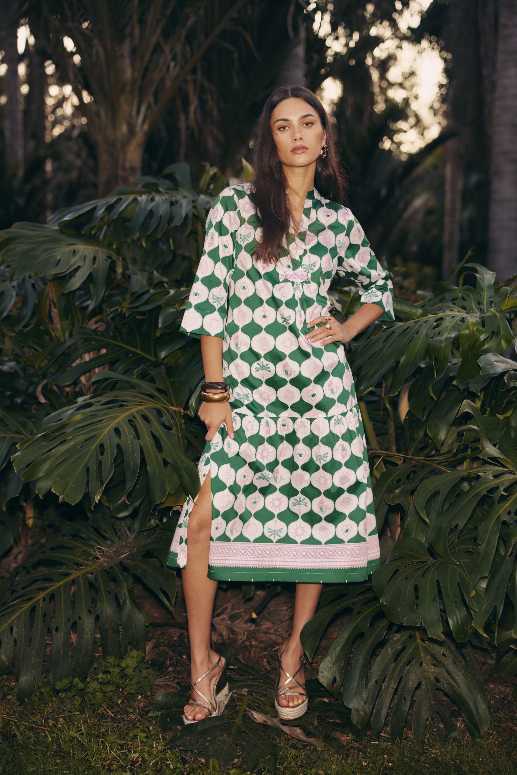 model wearing green and white midi dress standing among tropical plants