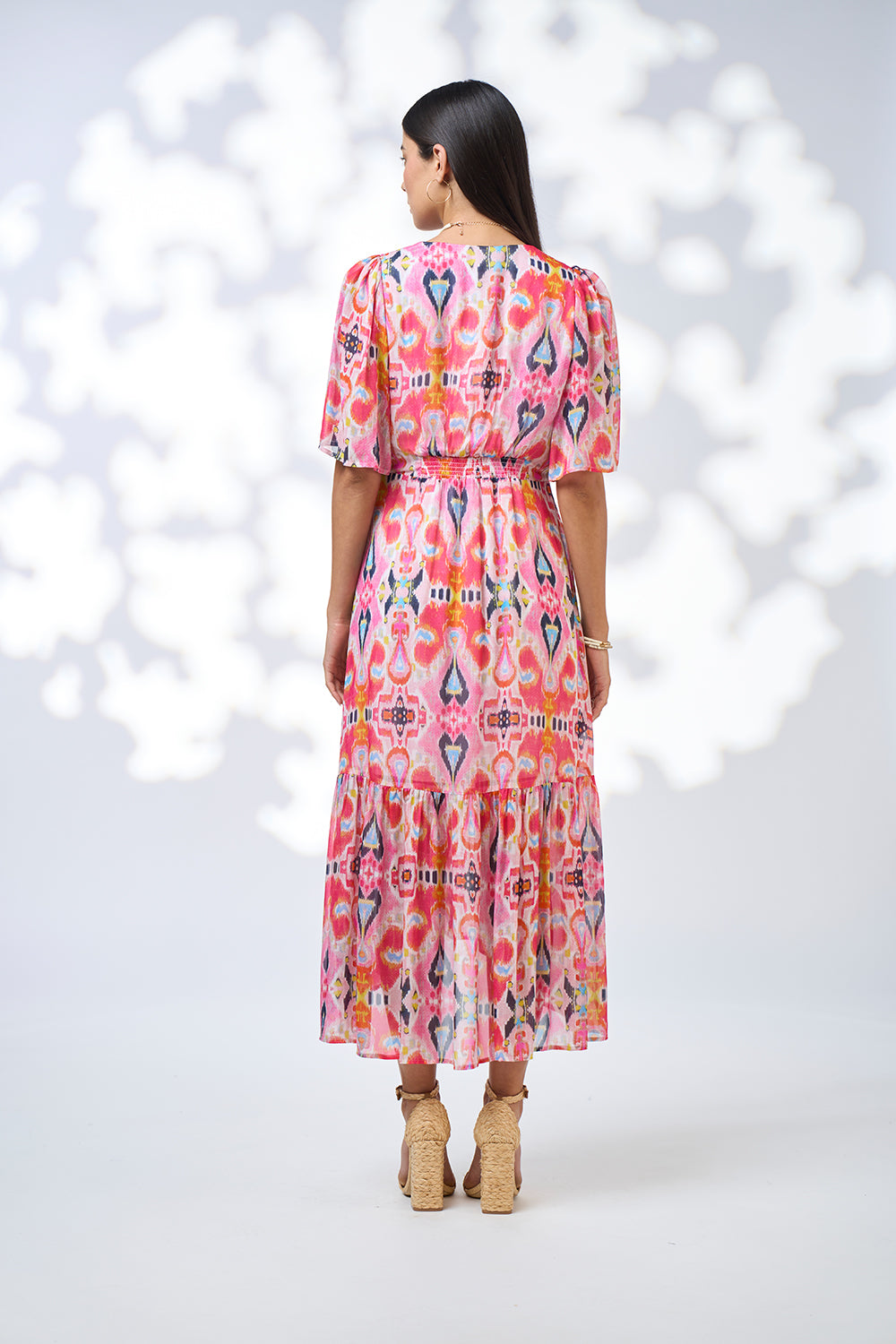 Woman wearing a colorful patterned dress on a white background back