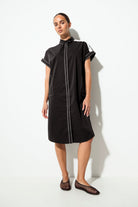 A woman modeling a black short-sleeve midi dress with contrasting light gray piping details, standing against a white studio background.