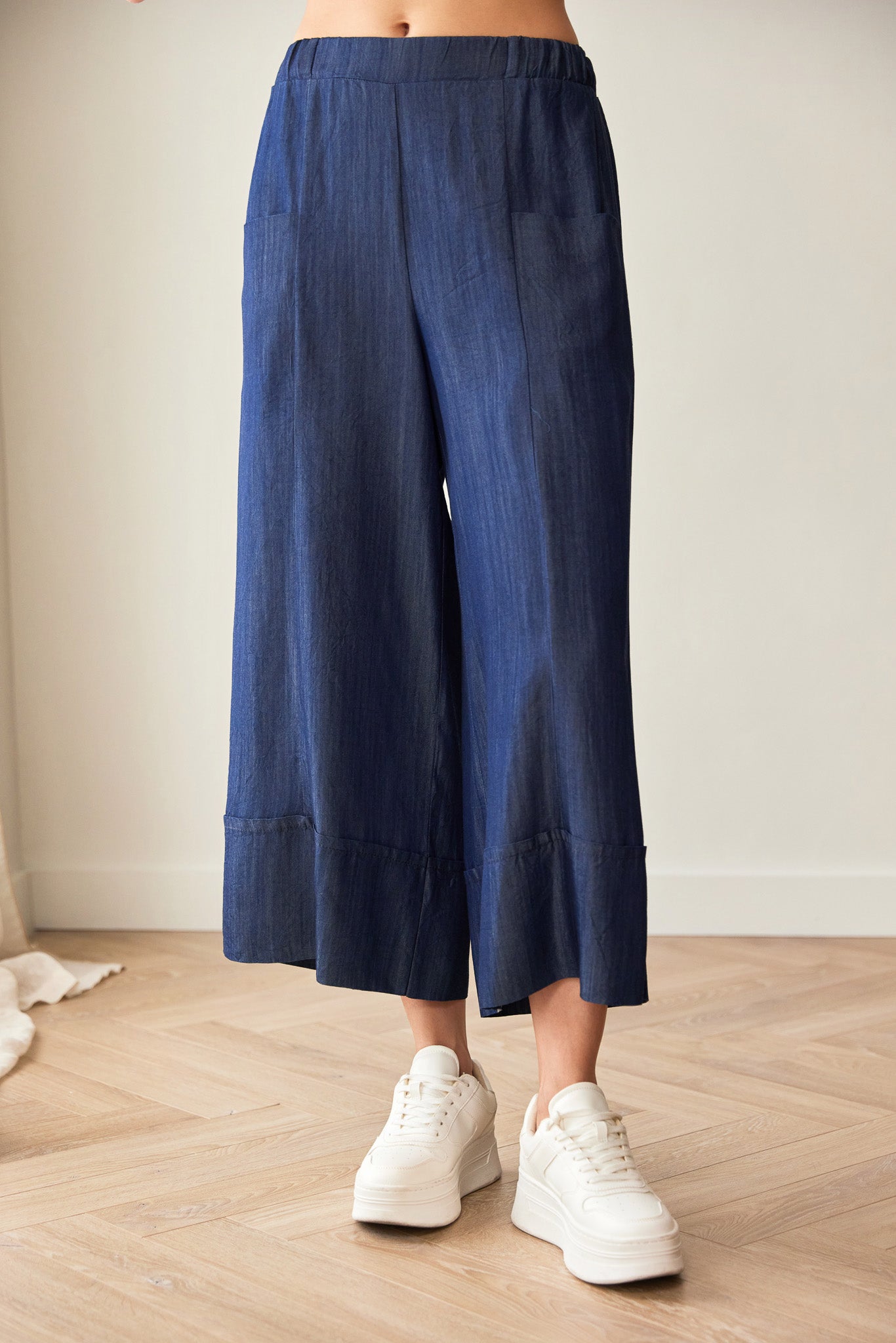 Person wearing blue wide-leg pants and white sneakers on a wooden floor.
