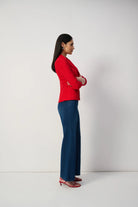 Woman wearing a red blazer and blue pants against a white background