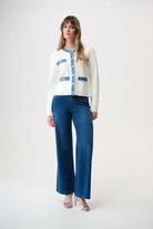 Woman wearing a white cardigan with blue accents and blue jeans on a white background